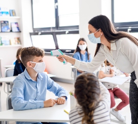 profesora con mascarilla toma temperatura a alumnos con termómetro digital en sala de clases